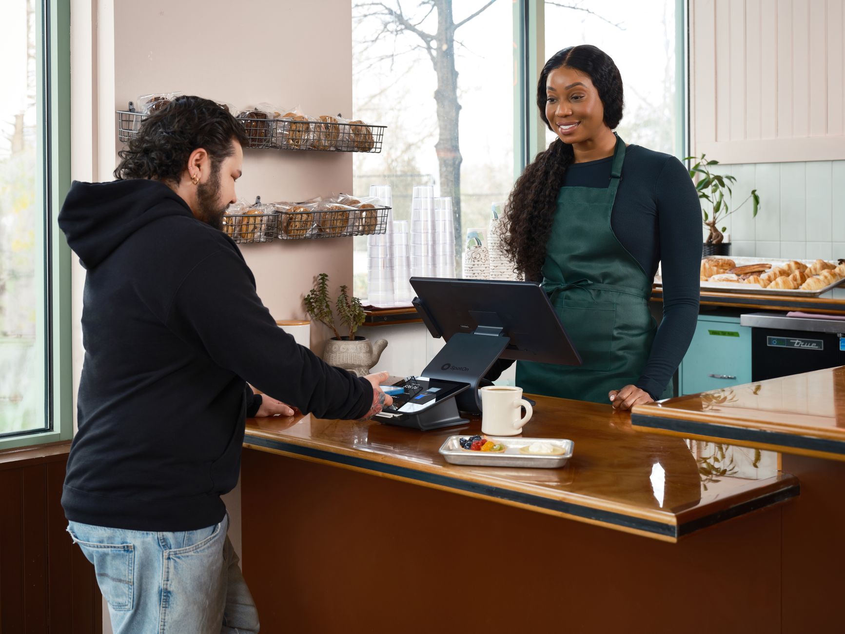 Customer holding a phone over a card reader at a coffee shop counter