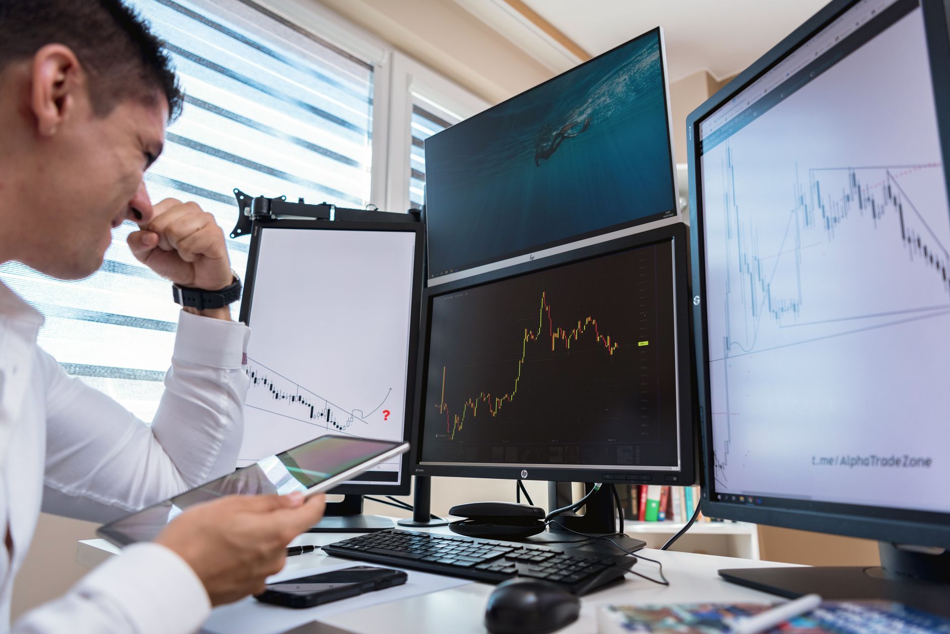 Trader seated at a desk watching candlestick charts across three computer monitors