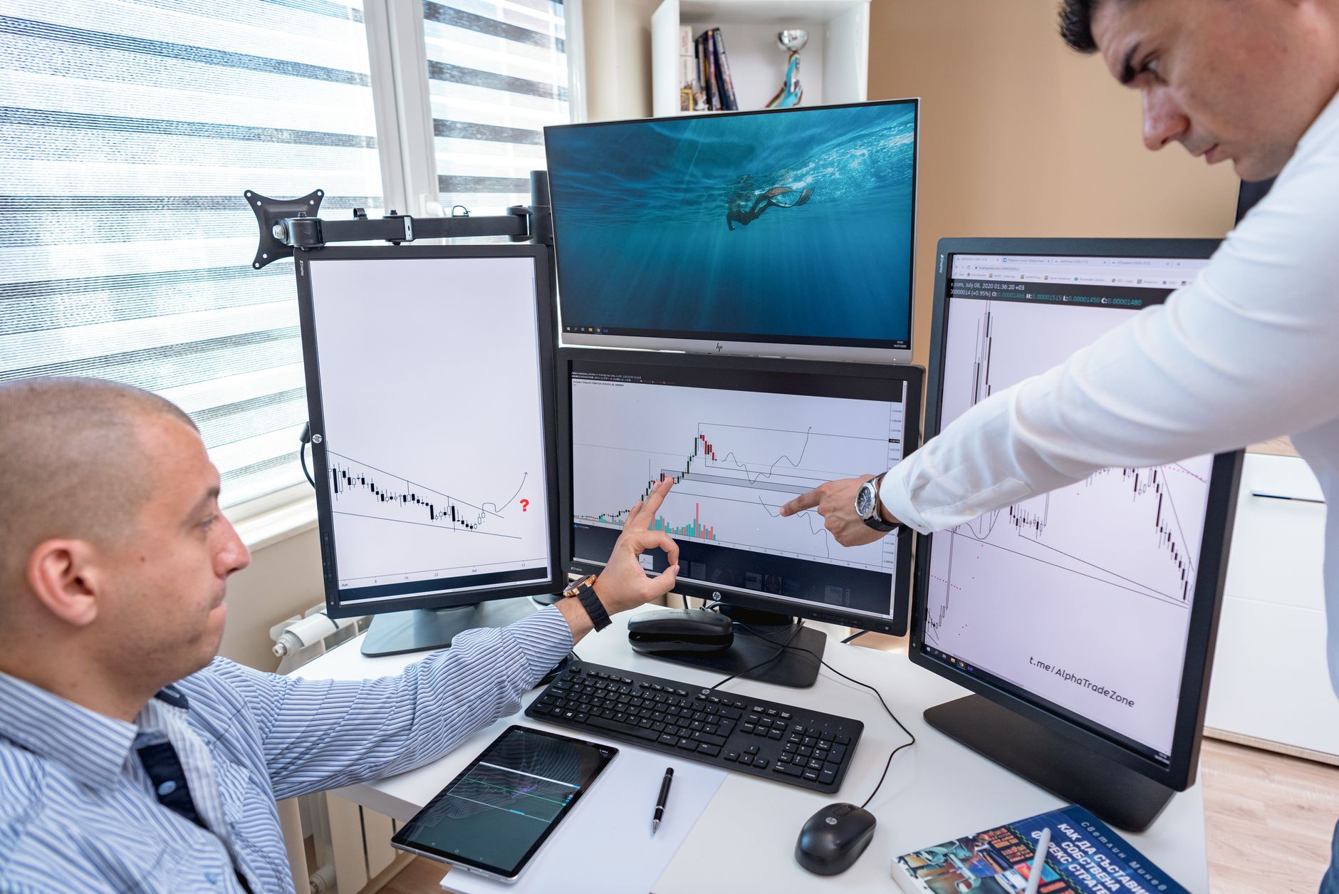Two people reviewing crypto price charts on computer monitors in an office