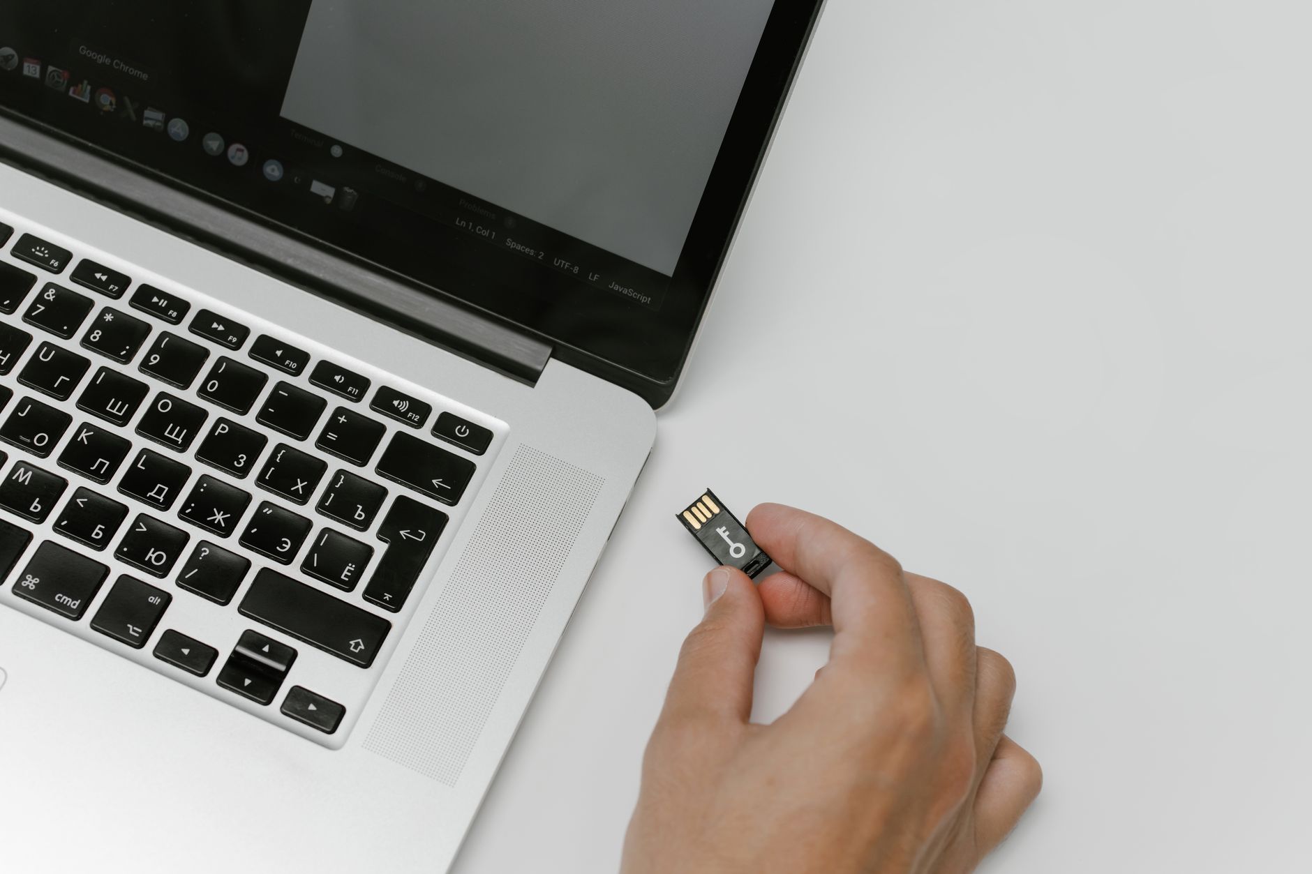 Person holding a small hardware wallet beside an open laptop on a desk